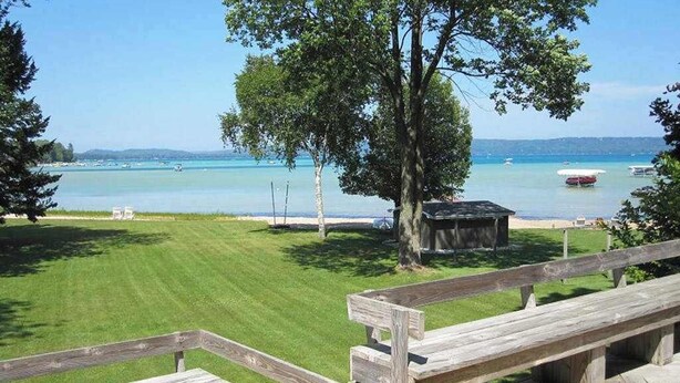 Ein Rasenplatz mit einer Holzterrasse, einem Picknicktisch und Blick auf einen See mit Booten.