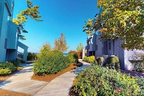 A modern building with a pathway leading to the entrance, surrounded by well-maintained greenery. - Lower-level beachfront condo with deck, fireplace, washer/dryer, central AC (Glen Arbor)