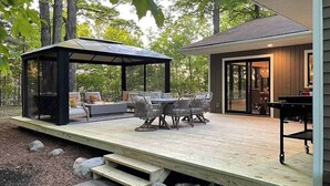 Un espacio al aire libre cubierto con mesas y sillas, una terraza de madera y un edificio con puertas de cristal.