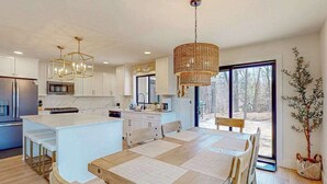 Una cocina moderna con armarios blancos, una isla central y una zona de comedor con mesa y sillas de madera.
