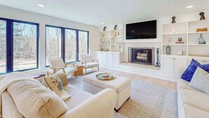 Una sala de estar moderna con chimenea, muebles blancos y ventanas amplias.