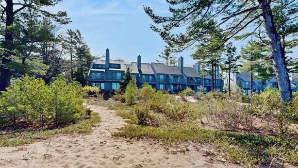 A row of modern buildings with a sandy path leading to them, surrounded by trees. - Desirable beachfront condo in Glen Arbor with patio, fireplace, kitchenette & AC (Glen Arbor)