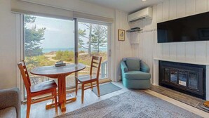 A modern living room with a fireplace, a television, and a large window offering a view of the outdoors. - Desirable beachfront condo in Glen Arbor with patio, fireplace, kitchenette & AC (Glen Arbor)
