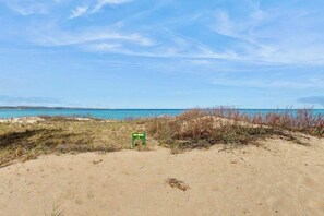 A beach with sand, sparse vegetation, and a clear sky. - Desirable beachfront condo in Glen Arbor with patio, fireplace, kitchenette & AC (Glen Arbor)