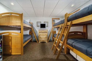 Une chambre avec des lits superposés en bois, une télévision, une commode et une échelle.
