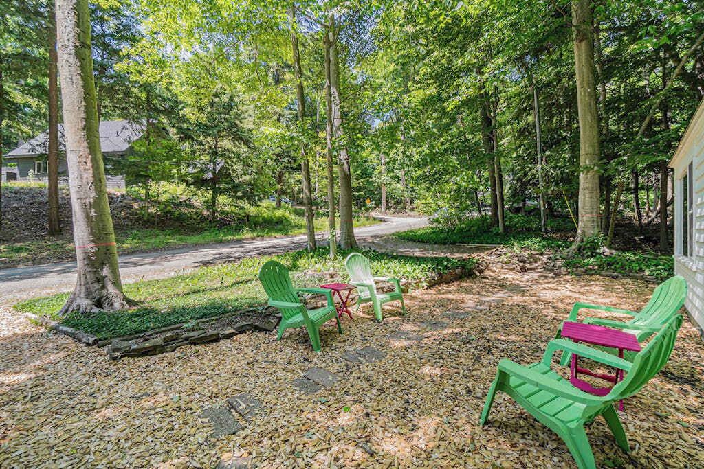 A forested area with a gravel path, green chairs, and a small table.