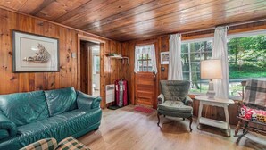 A wooden-paneled room with a green leather sofa, a chair, and a table with a lamp. - Peaceful & shady cottage near beach with streaming, free WiFi, full kitchen (Beulah)