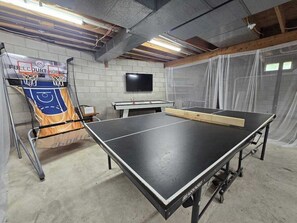 Ein Tischtennistisch, ein Kicker und ein Fernseher in einem Raum mit freiliegenden Decken und Betonwänden.