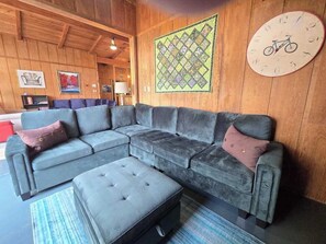 Ein Zimmer mit einem Ecksofa, einer runden Uhr im Fahrrad-Design und einer gesteppten Wandtextil.