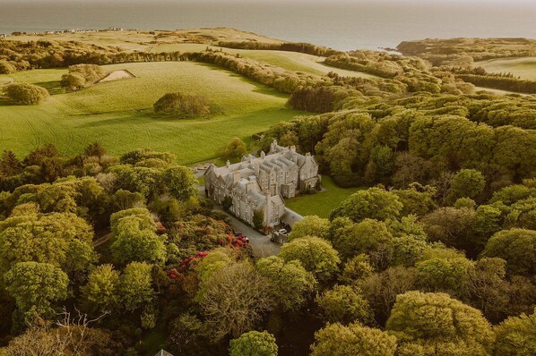 A large, historic building surrounded by lush greenery and rolling hills.