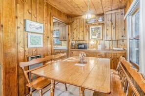 A wooden interior with a dining table, chairs, a kitchen area, and framed artwork.