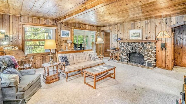 A log cabin interior with a stone fireplace, wooden walls, and a cozy seating area. - Lake home close to the water with WiFi, firepit, washer/dryer (Beulah)