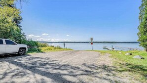 A gravel path leading to a lake with a dock, a white vehicle parked on the left, and a signpost in the distance. - Lake home close to the water with WiFi, firepit, washer/dryer (Beulah)