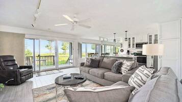 A modern living room with a sofa, armchair, and coffee table, connected to a kitchen area with cabinets and a dining space.
