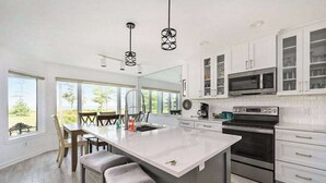 Une cuisine moderne dotée d’un grand îlot central, de meubles blancs, d’appareils électroménagers en acier inoxydable et d’un coin repas offrant une vue agréable.