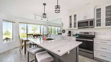 A modern kitchen with a large island, white cabinetry, stainless steel appliances, and a dining area with a view.