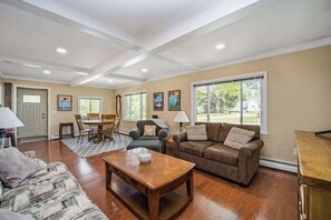A spacious living room with hardwood floors, a dining area, and a large window offering a view of the outdoors. - Stone home two blocks from the lake & downtown with gas grill & free Wi-Fi (Boyne City)