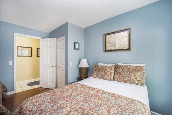 A bedroom with a bed, a door, a lamp, and a framed map on the wall. - Stone home two blocks from the lake & downtown with gas grill & free Wi-Fi (Boyne City)