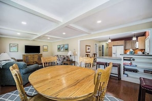 A dining area with a round wooden table and chairs, a sofa, and a television in the background. - Stone home two blocks from the lake & downtown with gas grill & free WiFi (Boyne City)