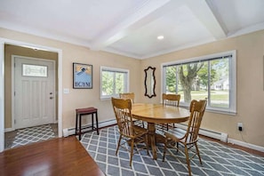 A dining room with a round table, wooden chairs, a mirror, and windows with a view of trees. - Stone home two blocks from the lake & downtown with gas grill & free WiFi (Boyne City)