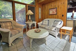 A room with wicker furniture, a round table, and a view through large windows. - Spacious vacation gem on Crystal Lake w/gas fireplace, WiFi, central AC, firepit (Frankfort)