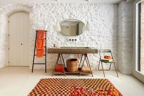 Un baño con pared de piedra, un espejo redondo, un lavabo, una escalera y una silla.