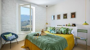 Un dormitorio con cama, una silla, un ventanal y una pared decorada con marcos.