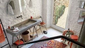 Un baño con lavamanos de piedra, un espejo, luces colgantes, una ventana con vistas y una alfombra estampada.