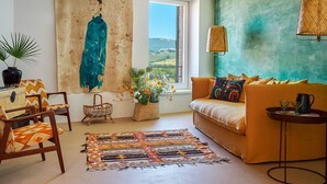 Una sala de estar con un sofá, sillas, un cuadro grande, un ventanal con vistas y una lámpara colgante.