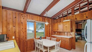Ein Holzblockhaus-Interieur mit Esstisch, Stühlen, einer Küchenzeile und Blick ins Freie.
