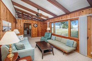 Un intérieur en bois avec un canapé, un fauteuil et une table basse, de grandes fenêtres et un ventilateur de plafond.
