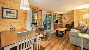 L’intérieur chaleureux d’un chalet avec des murs en bois, une table à manger, un canapé et un téléviseur.