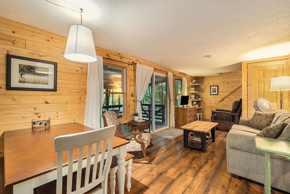 A cozy cabin interior with wooden walls, a dining table, a sofa, and a television.