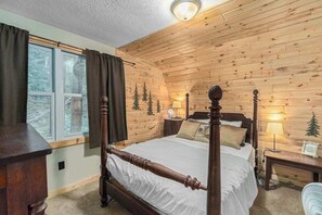 A wooden-paneled bedroom with a four-poster bed, a nightstand with a lamp, and a window with curtains.