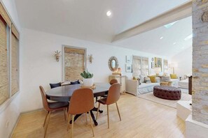 A dining area with a table and chairs, a potted plant, and a sofa in the background.