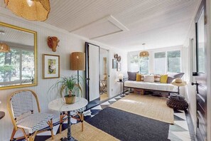 A room with a bed, a dining table, and a chair. There is a window with a view of trees.