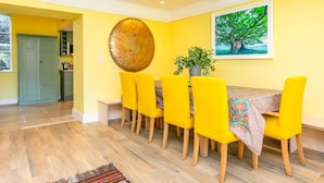 A dining area with yellow chairs, a table with a floral tablecloth, a large abstract wall art, and a potted plant. - Heatherstone House - Six Bedroom Villa, Sleeps 10 (Broughton)