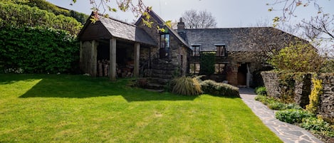 Une maison en pierre avec un toit en pente, un chemin en pierre et une pelouse bien entretenue.
