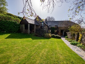 Una casa de piedra con techo inclinado, un camino de piedras y un césped bien cuidado.