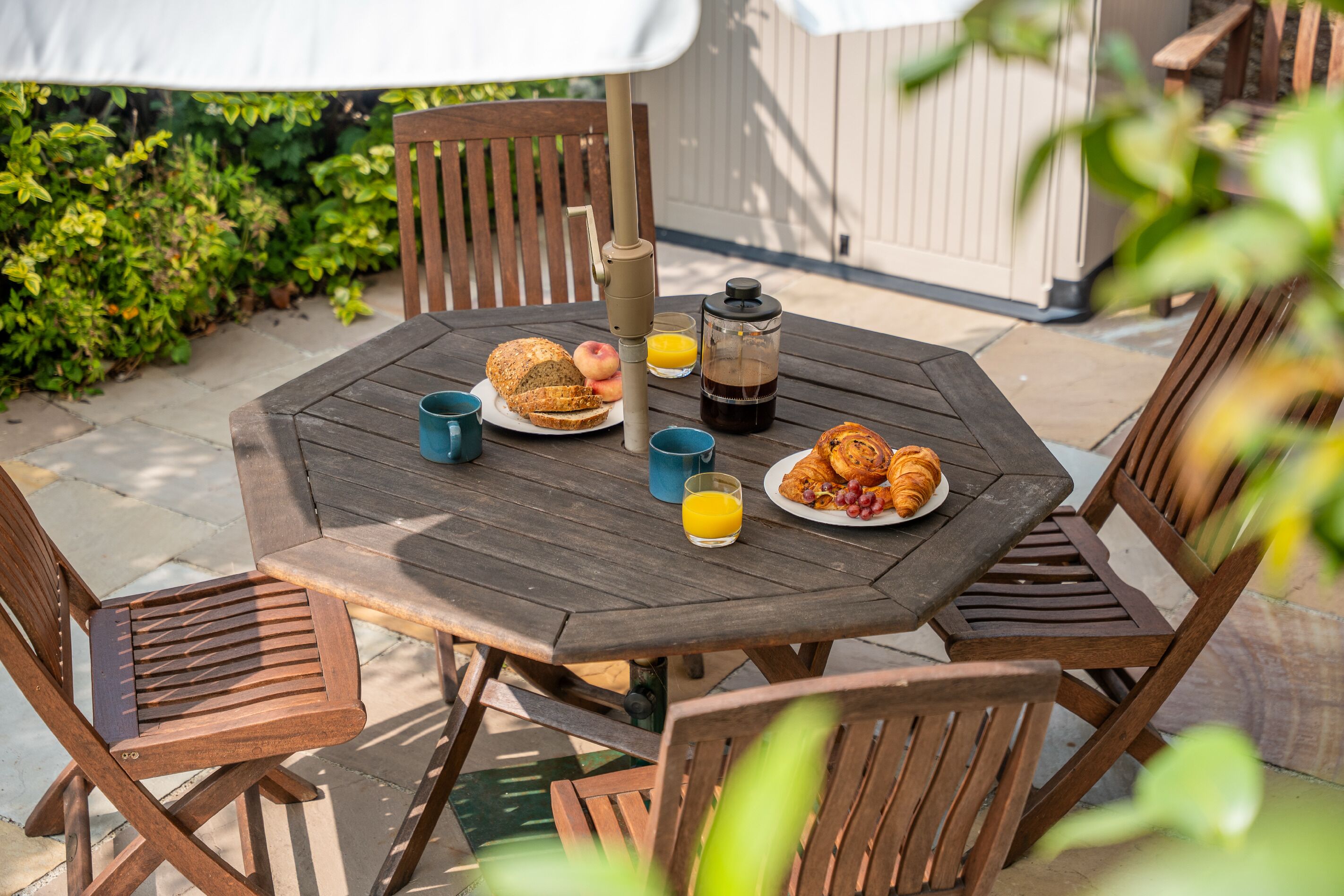 Une table en bois sur laquelle sont disposés des aliments pour le petit-déjeuner, notamment du pain, des fruits et une machine à café.
