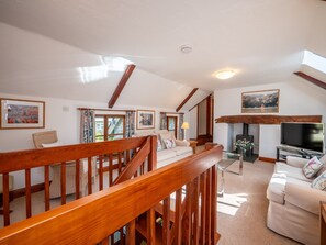 Un salón espacioso con una escalera de madera, chimenea, televisor y cuadros en las paredes.