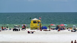 Ein Strand mit einem Rettungsturm, Sonnenschirmen und entspannten Personen.