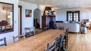 A dining area with a long wooden table, chairs, a brick fireplace, and a sofa in the background. - Family-friendly Home w/ Lake Views, Free WiFi & Private Beach Access (Union Pier)