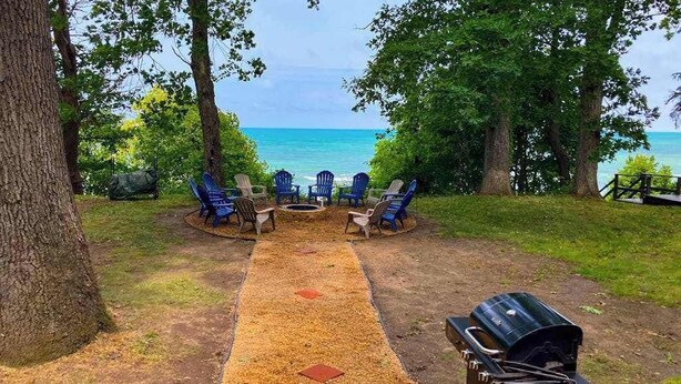 A patio with outdoor seating and a grill, overlooking a body of water. - Family-friendly Home w/ Lake Views, Free WiFi & Private Beach Access (Union Pier)