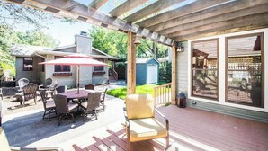 Un patio couvert avec des meubles d’extérieur, un barbecue et une vue sur une maison.