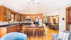 Une cuisine moderne avec des meubles en bois, un îlot central doté de tabourets et un coin repas avec une table et des chaises.