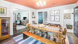 A dining area with a wooden table, chairs, and a bench. There are framed pictures on the walls and a cabinet with glass doors.
