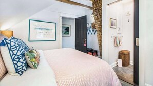 A bedroom with a sloped ceiling, a bed with patterned bedding, a framed picture on the wall, and a door leading to another room.