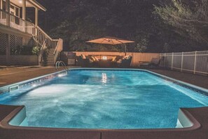 A rectangular swimming pool with a wooden deck surrounding it, a covered seating area with an umbrella, and a staircase leading to a covered porch. - Dog-friendly house with private heated outdoor pool, hot tub & Ping-Pong (Grand Beach)