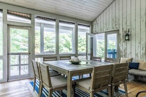 Une table à manger en bois, avec des chaises, un banc et une vue dégagée grâce à de grandes fenêtres.
